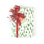 Front view of gift wrapped in green brushstroke wrapping paper with red ribbon and ornament tag.