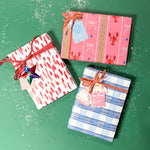 Three christmas gifts wrapped in colorful christmas wrapping paper from Madcap Cottage on a green background.