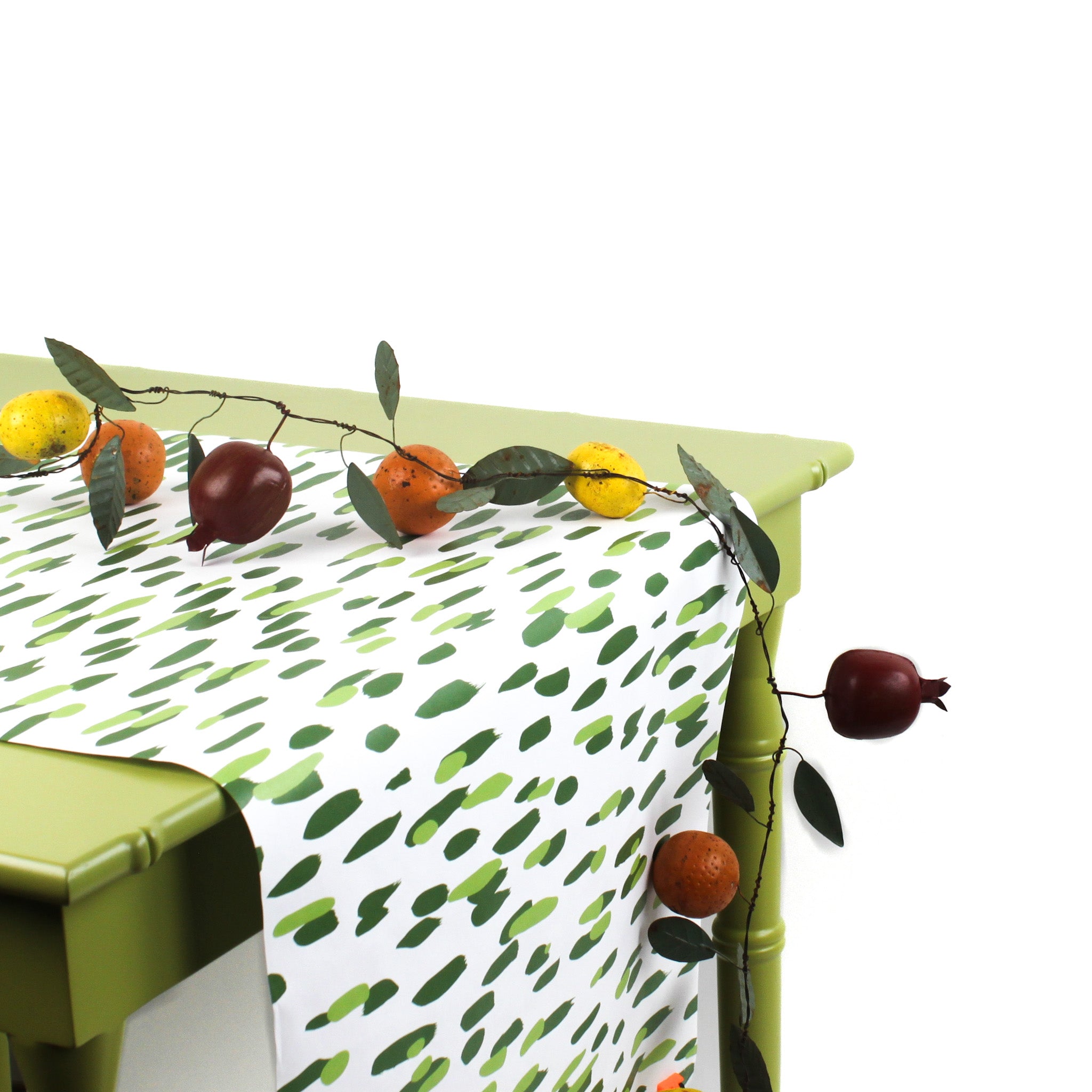a green table covered with a green and white paper table runner with a brushtroke pattern and a fruit garland on top