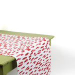 a green table covered by a white and red paper table runner featuring a brushtroke pattern called Club House by Madcap Cottage