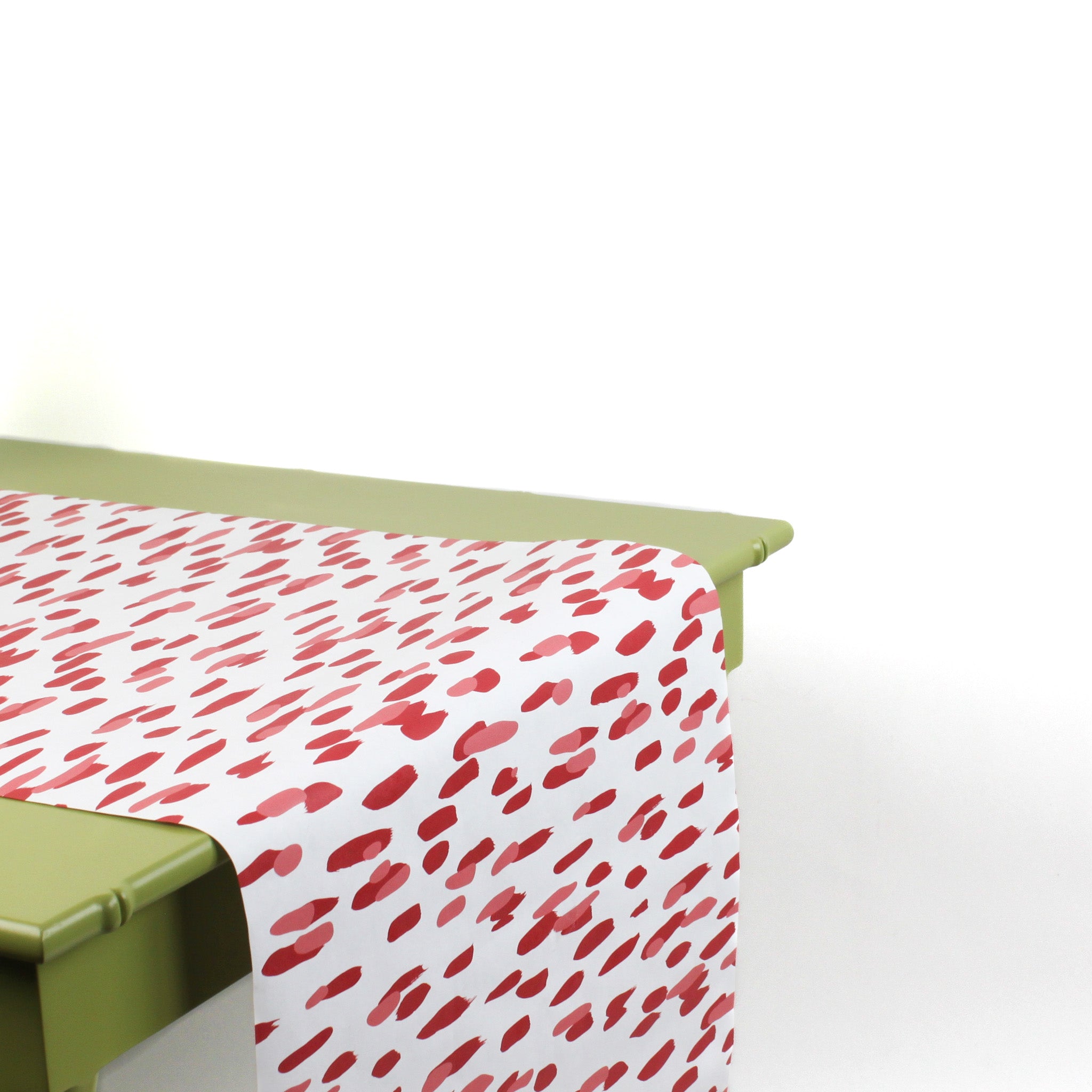 a green table covered by a white and red paper table runner featuring a brushtroke pattern called Club House by Madcap Cottage