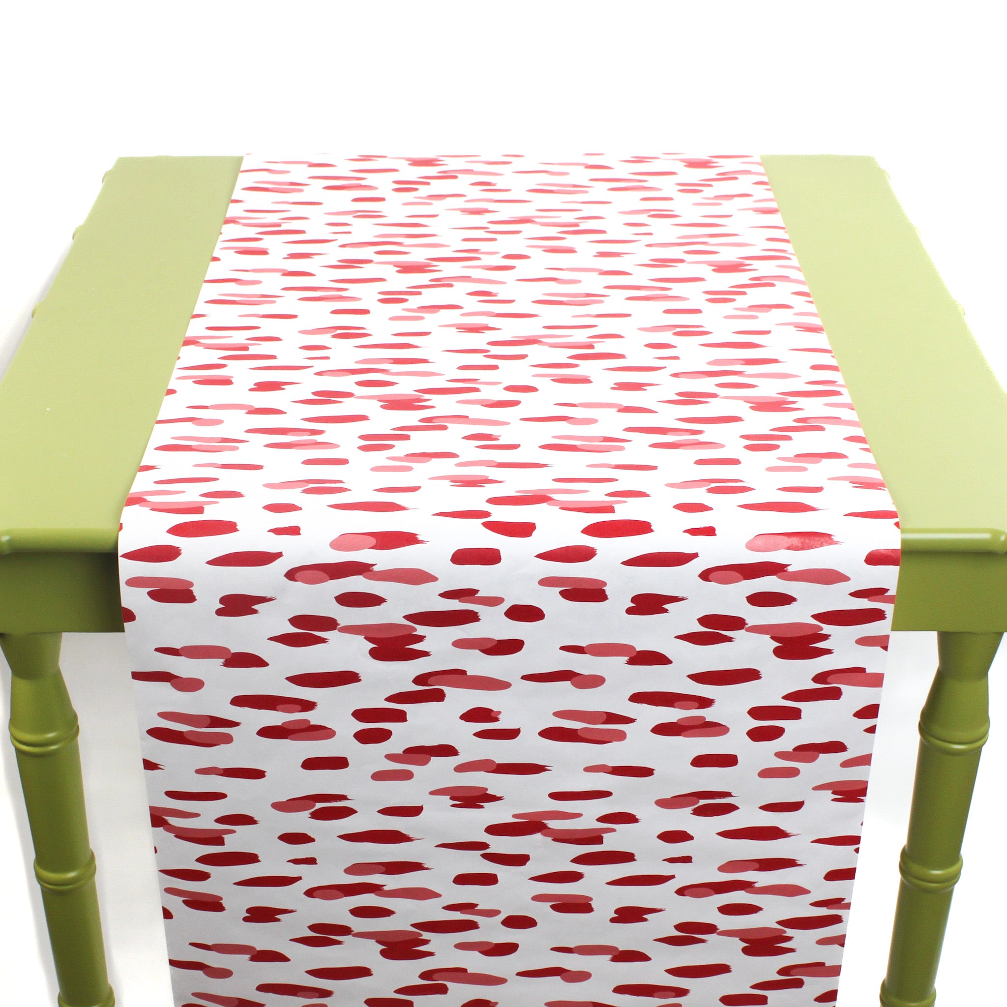 a green table covered by a white and red paper table runner featuring a brushtroke pattern called Club House by Madcap Cottage