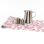 Clubhouse red paper table runner styled with striped pitcher and matching cups.