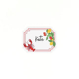 Coastal themed place card featuring lobster, lemons, and strawberries with a handwritten name on a white background.
