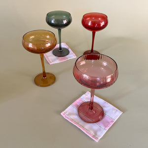 colored coupe glasses with cocktail napkins