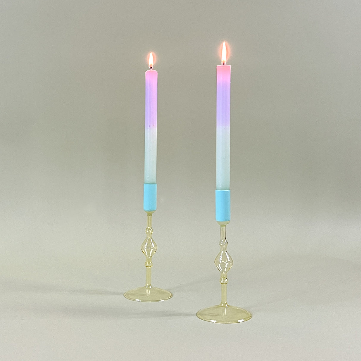 two yellow colored glass candle holders with blue tops holding pastel taper candles