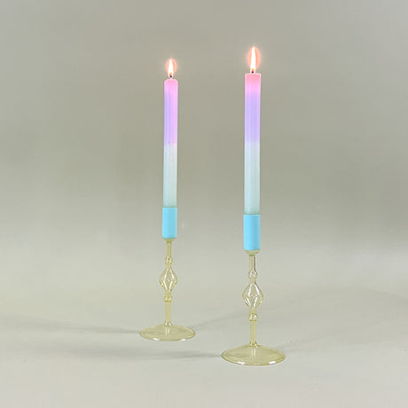 two yellow colored glass candle holders with blue tops holding pastel taper candles