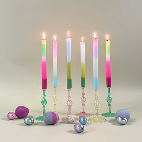 six colored glass candle holders in pink, yellow and green holding pastel taper candles. 