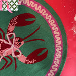 A round green rug with a central lobster motive and a pink ribboned border.