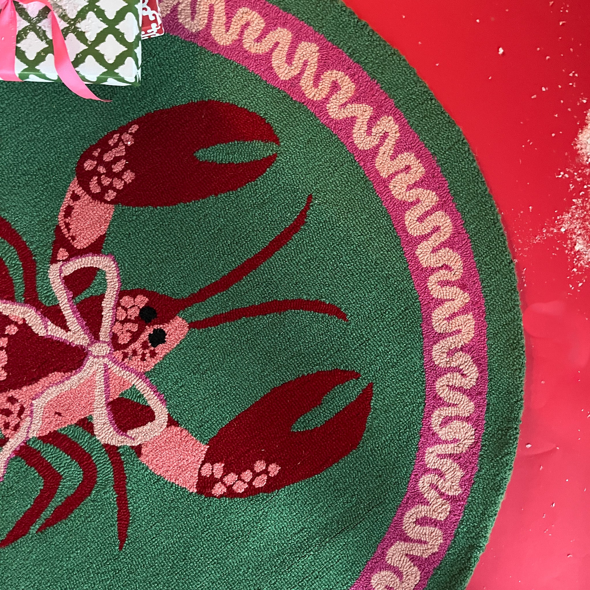 A round green rug with a central lobster motive and a pink ribboned border.