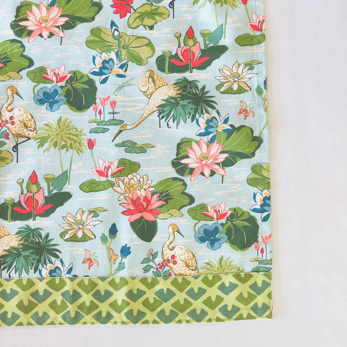 corner view of a floral tea towel from madcap cottage featuring herons and water lilites. 