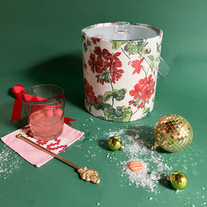 Cottage Grove Geranium is an acrylic ice bucket covered in red geranium fabric and surrounded by a cocktail and festive decorations.