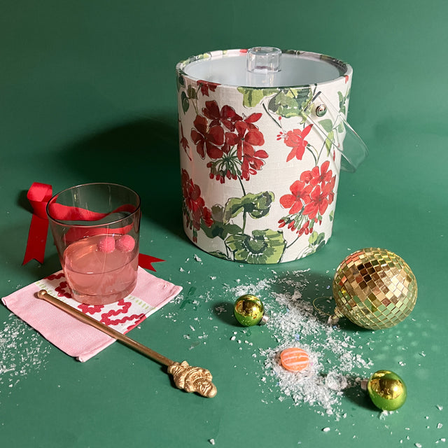 Cottage Grove Geranium is an acrylic ice bucket covered in red geranium fabric and surrounded by a cocktail and festive decorations.