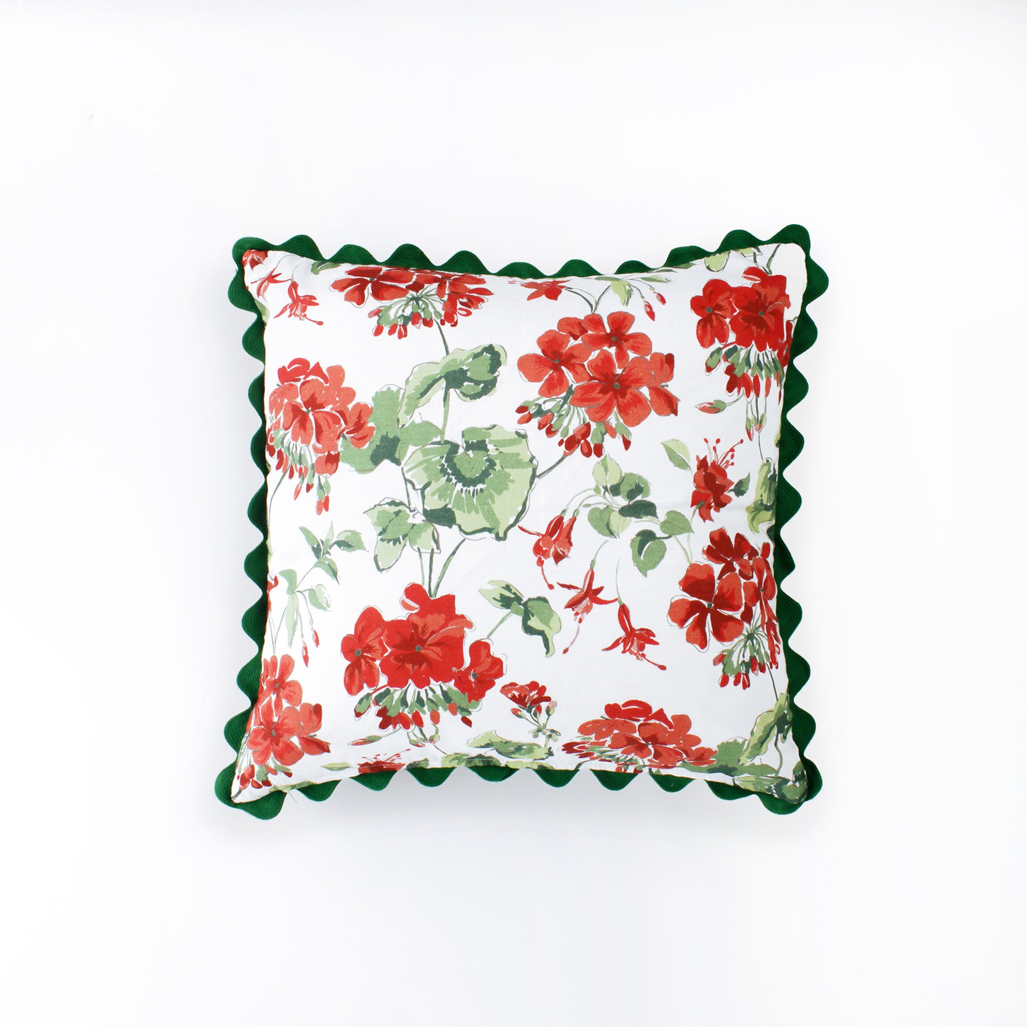 Square decorative pillow featuring a red and green floral geranium pattern on a white background, finished with a dark green scalloped trim around the edges.