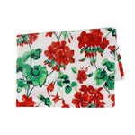 a white floral tea towel featuring a pattern of red geranium motifs against a white background. 