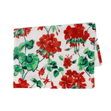 a white floral tea towel featuring a pattern of red geranium motifs against a white background. 