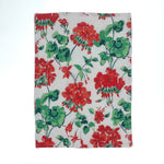 a white floral tea towel featuring a pattern of red geranium motifs against a white background. 