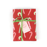 Front view of gift wrapped in red candy cane wrapping paper with green ribbon and pink gift tag.
