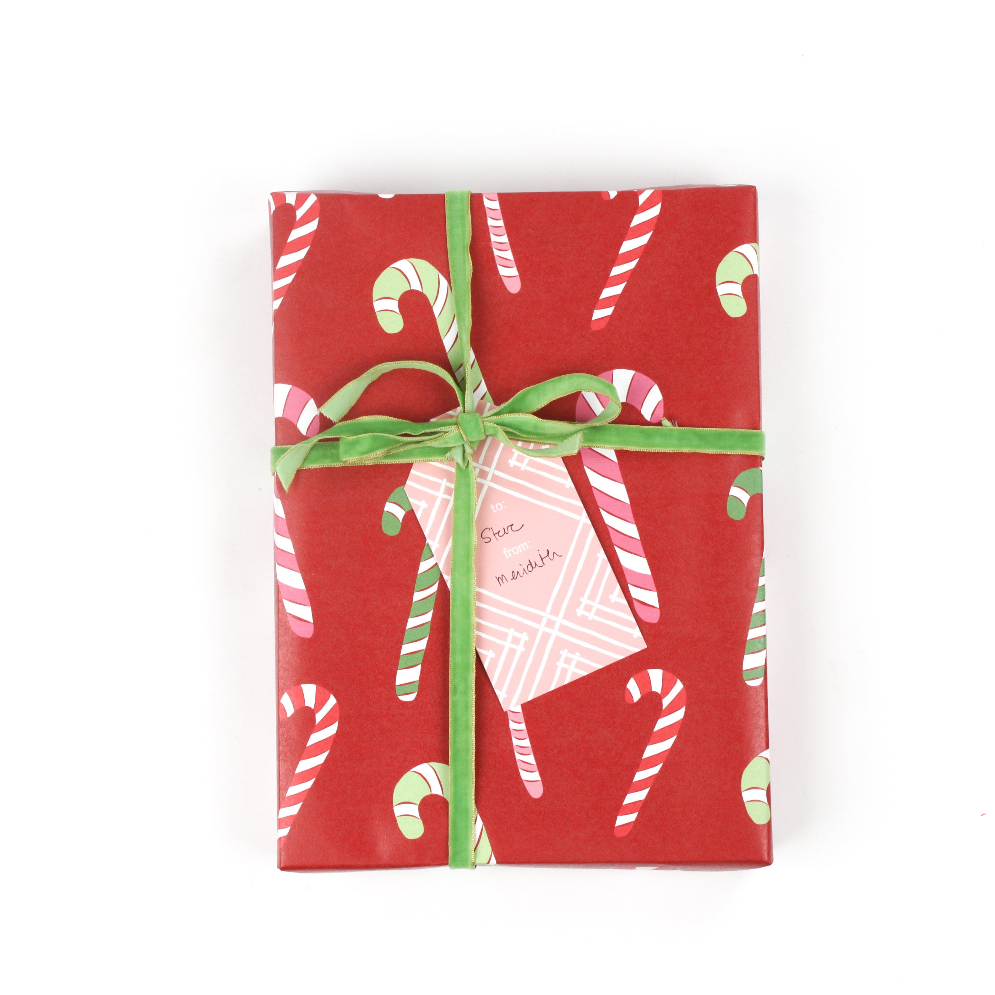 Front view of gift wrapped in red candy cane wrapping paper with green ribbon and pink gift tag.