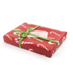 Side view of gift wrapped in red candy cane wrapping paper with green ribbon.
