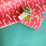 Styled display of red candy cane wrapping paper with green ribbon and gift tag.