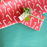 Styled display of red candy cane wrapping paper with green ribbon and gift tag.
