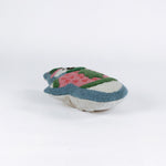 Snowman-shaped decorative pillow with a hooked texture, featuring a smiling snowman wearing a pink sweater with a green Christmas tree design and a matching blue and pink hat lying in a white surface