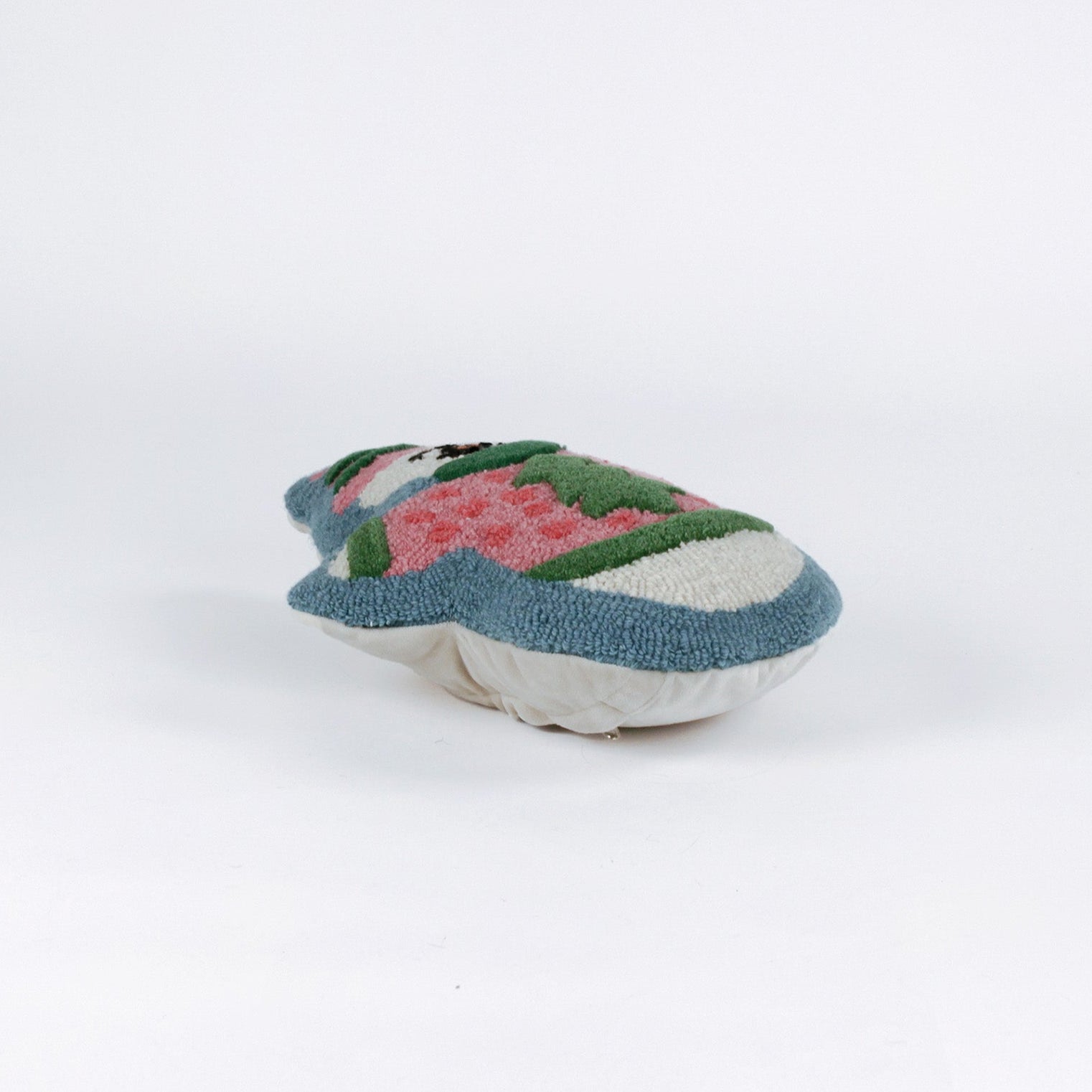 Snowman-shaped decorative pillow with a hooked texture, featuring a smiling snowman wearing a pink sweater with a green Christmas tree design and a matching blue and pink hat lying in a white surface