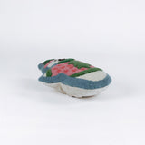 Snowman-shaped decorative pillow with a hooked texture, featuring a smiling snowman wearing a pink sweater with a green Christmas tree design and a matching blue and pink hat lying in a white surface