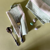 two green gingham dinner napkins in gin lane print fabric by madap cottage next to cutlery and small easter eggs on a green background