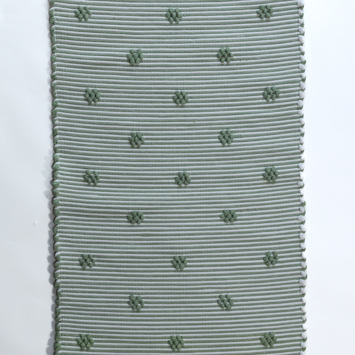 A rectangular green accent rug with small daisy shaped accents scattered across it. 