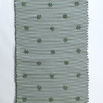 A rectangular green accent rug with small daisy shaped accents scattered across it. 