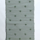 A rectangular green accent rug with small daisy shaped accents scattered across it. 