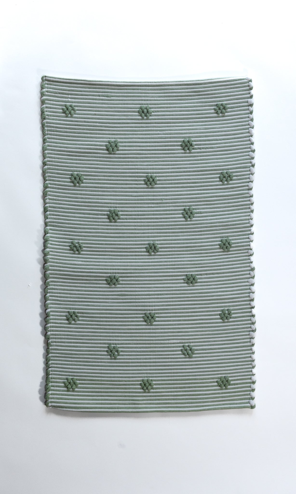 A rectangular green accent rug with small daisy shaped accents scattered across it. 