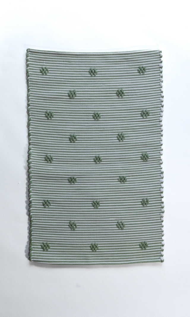 A rectangular green accent rug with small daisy shaped accents scattered across it. 