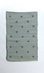 A rectangular green accent rug with small daisy shaped accents scattered across it. 