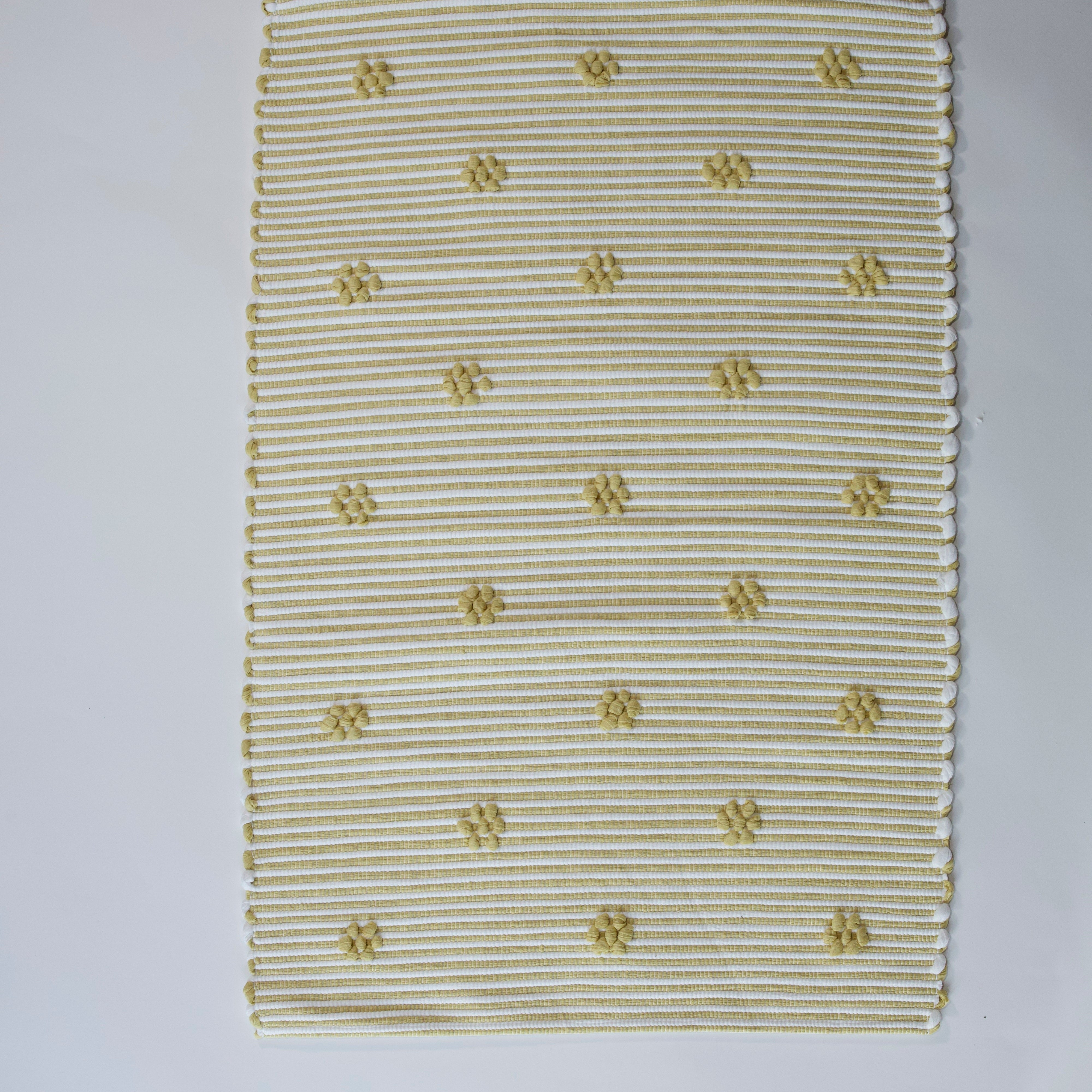 A rectangular yellow accent rug with small daisy shaped accents scattered across it. 
