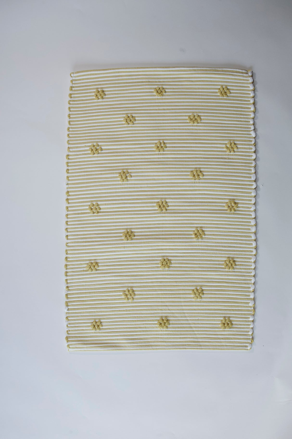 A rectangular yellow accent rug with small daisy shaped accents scattered across it. 