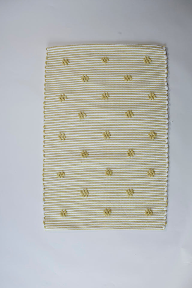 A rectangular yellow accent rug with small daisy shaped accents scattered across it. 