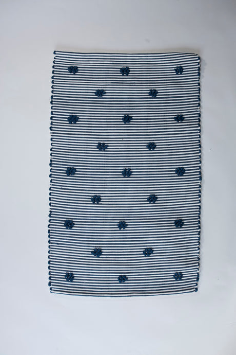 A rectangular navy blue accent rug with small daisy shaped accents scattered across it. 