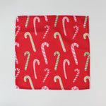 Red Christmas dinner napkin featuring an allover candy cane pattern in red, pink, green, and white, finished with stitched edges for festive holiday kitchen décor.
