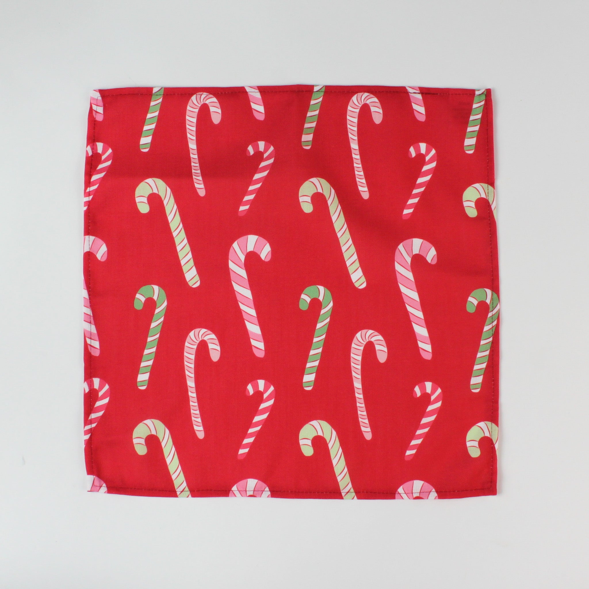 Red Christmas dinner napkin featuring an allover candy cane pattern in red, pink, green, and white, finished with stitched edges for festive holiday kitchen décor.