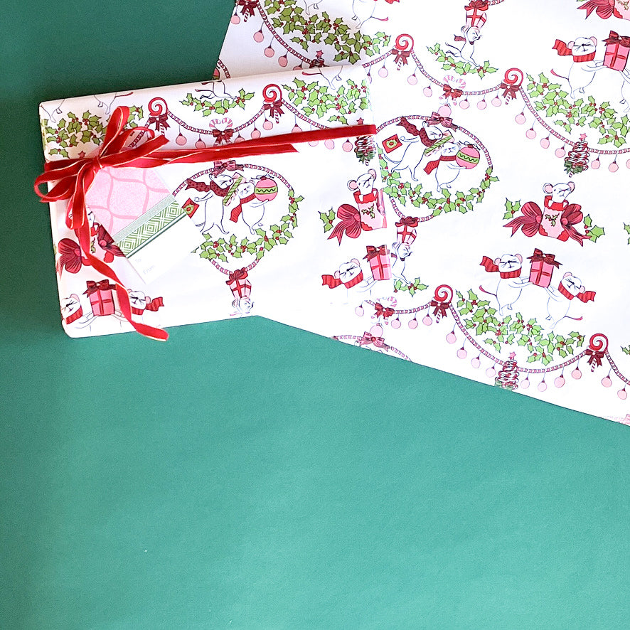Styled flat lay of mouse-themed holiday wrapping paper with red ribbon and gift tag.