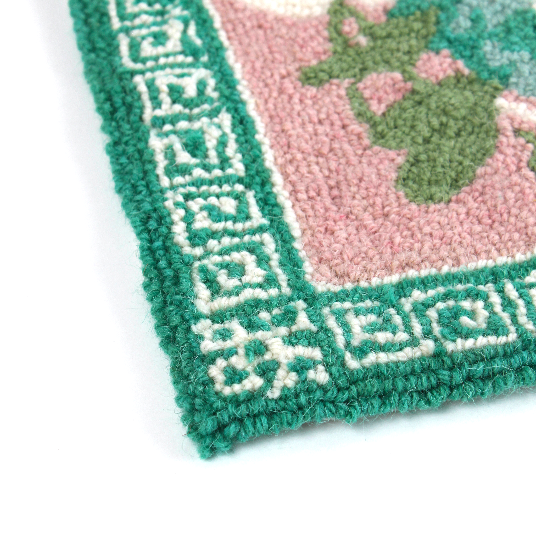 close up detail of a green and pink rug with a green pug motif and a green geometric border