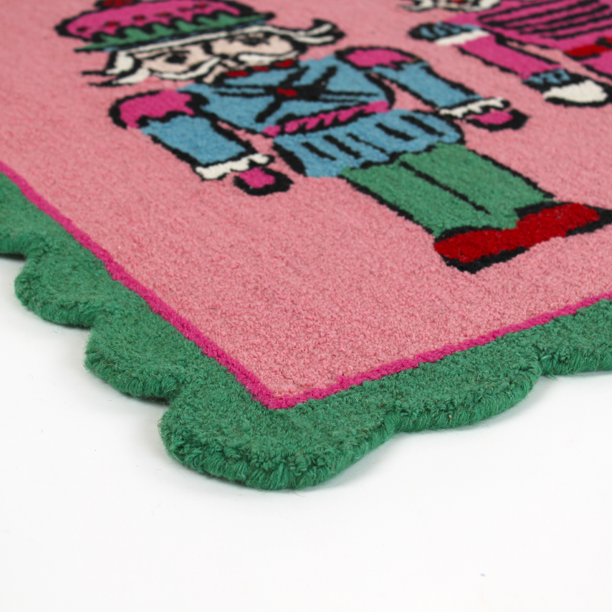 close up of a PInk and green christmas rug featuring three nutcrackers and a green scalloped border