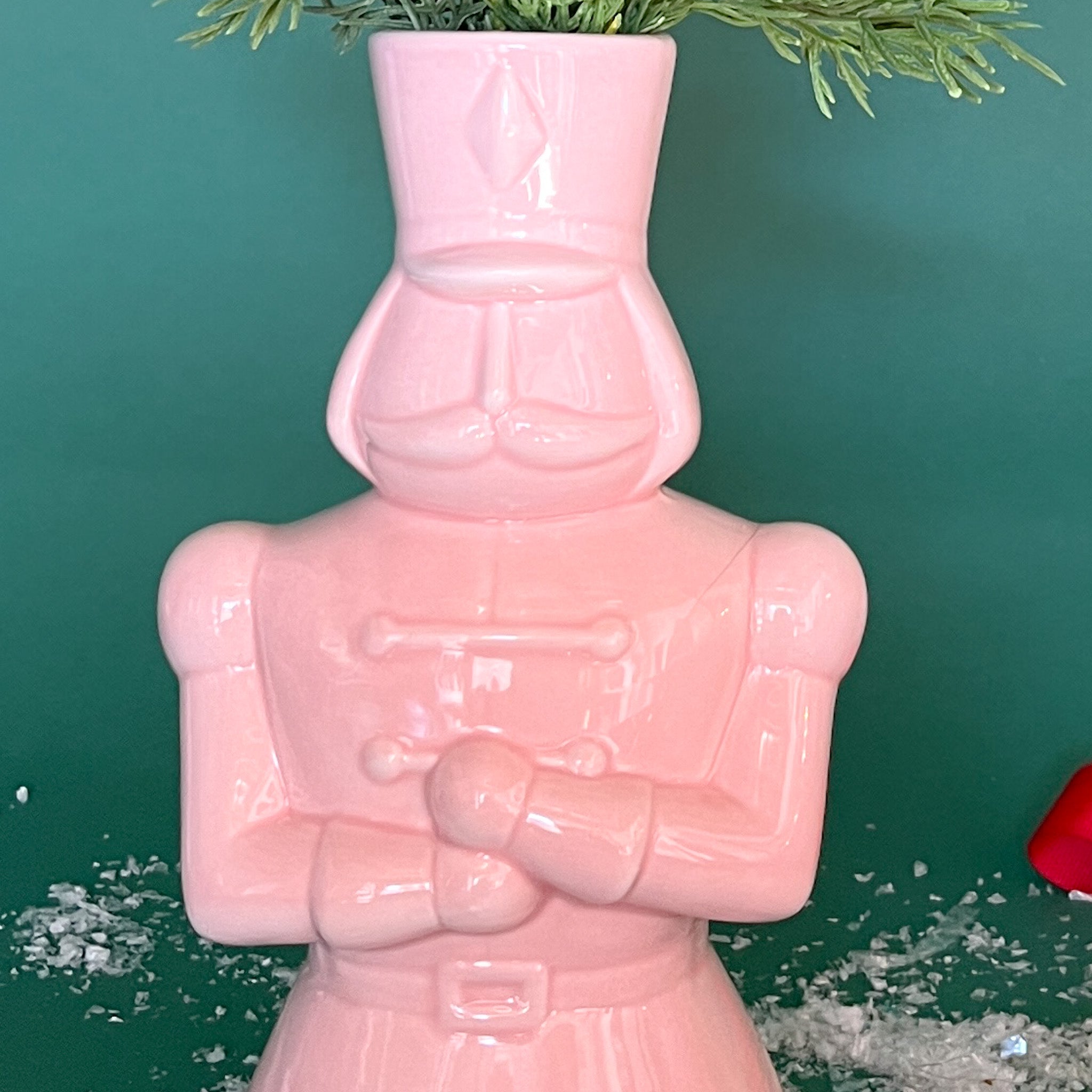 a close up shot of a nutcracker shaped pink ceramic christmas vase against a green, christmassy background. 