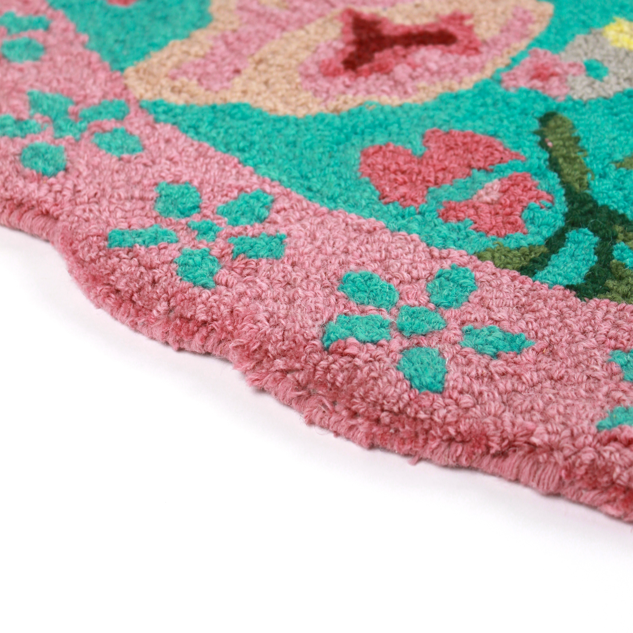 close up details of A pink and green floral rug featuring a scalloped border and large central pug motif
