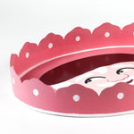 close up look of a Hand-Painted Metal Christmas Santa Tray featuring a cheerful Santa Claus face with a red hat on a pink circular background with scalloped edges.
