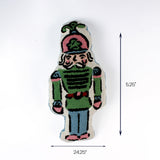 Nutcracker-shaped decorative pillow in green blue and pink tones shown with 24.25 inch length and 5.25 inch height.
