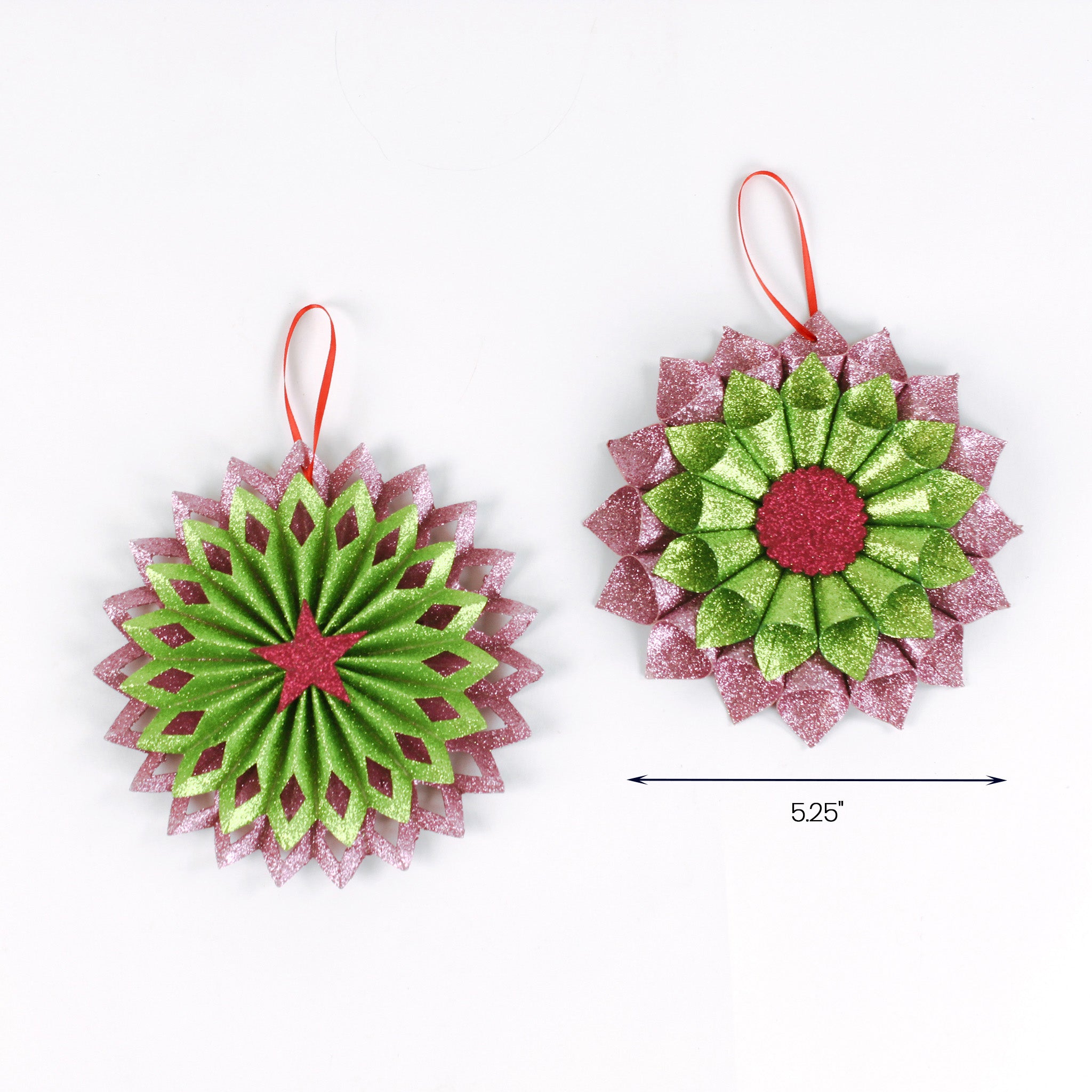 Two glittery flower-shaped Christmas ornaments in pink and green, each with a hanging loop, displayed side by side with a width measurement of 5.25 inches.